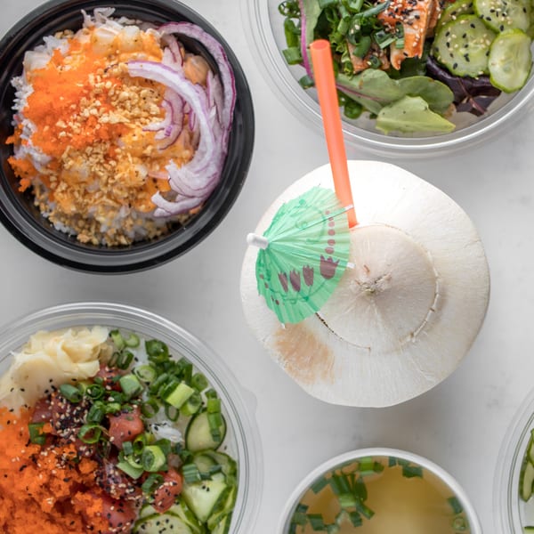 Overhead view of Hi Poke bowls with various toppings, soup, and a coconut drink.