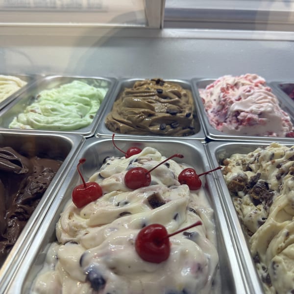 Assorted ice cream flavors in metal containers, including chocolate, mint, cherry, and coffee.