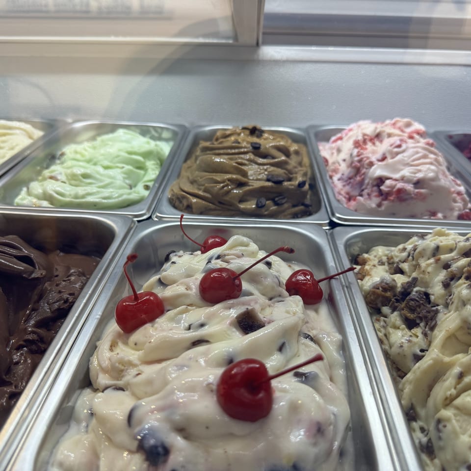 Assorted ice cream flavors in metal containers, including chocolate, mint, cherry, and coffee.