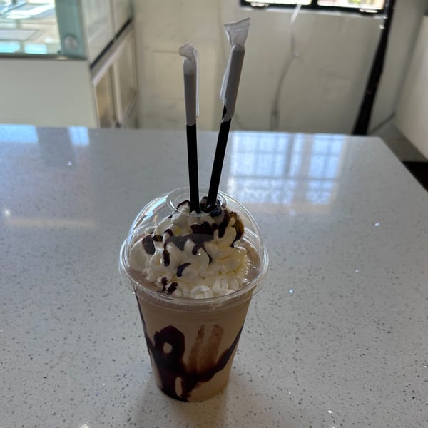 A Hi Poke iced coffee drink with whipped cream, chocolate drizzle, and two straws on a counter.