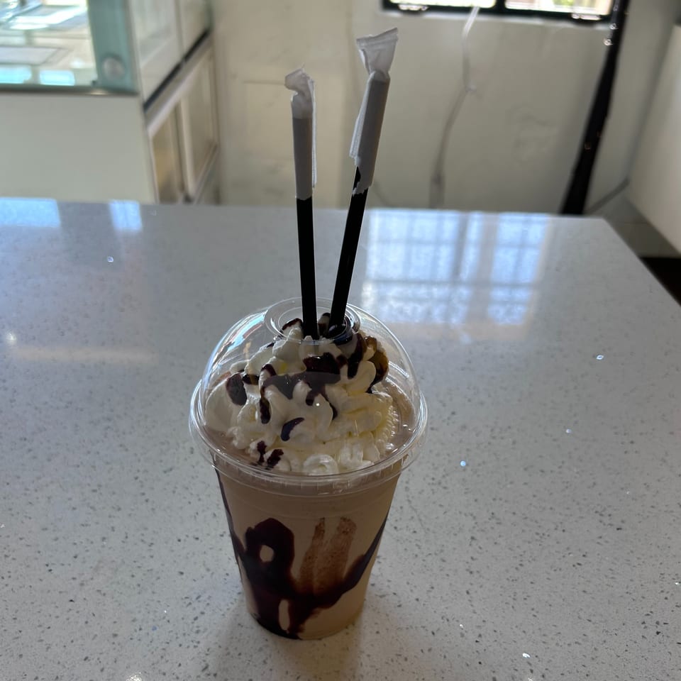 A Hi Poke iced coffee drink with whipped cream, chocolate drizzle, and two straws on a counter.