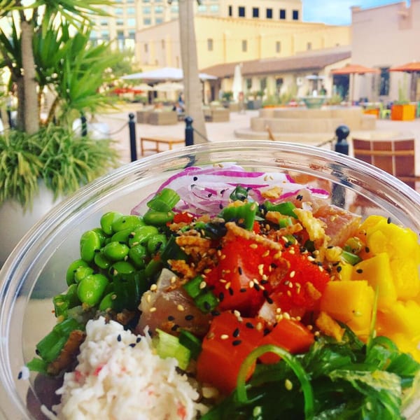 A vibrant Hi Poke bowl with tuna, mango, edamame, and seaweed, set against an outdoor patio.