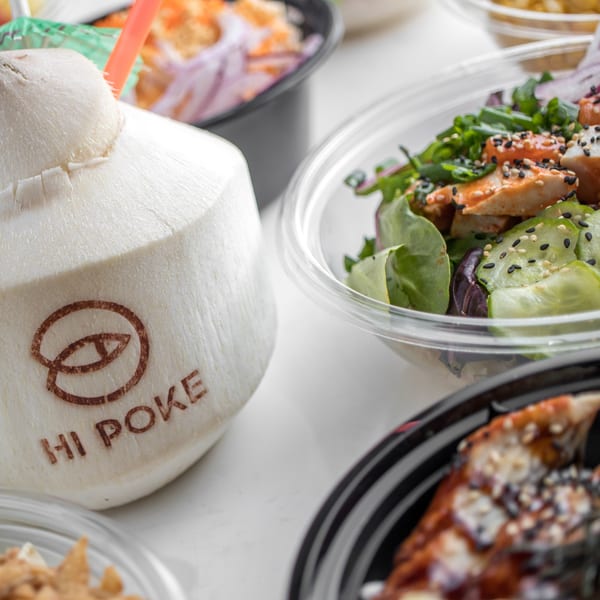 A Hi Poke branded coconut drink with a straw next to several poke bowls.