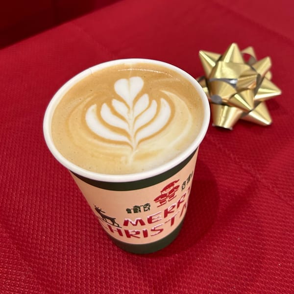 A Christmas-themed coffee cup with latte art on a red background with a gold bow.