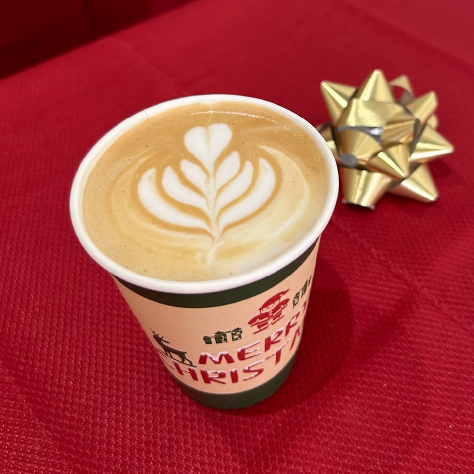 A Christmas-themed coffee cup with latte art on a red background with a gold bow.